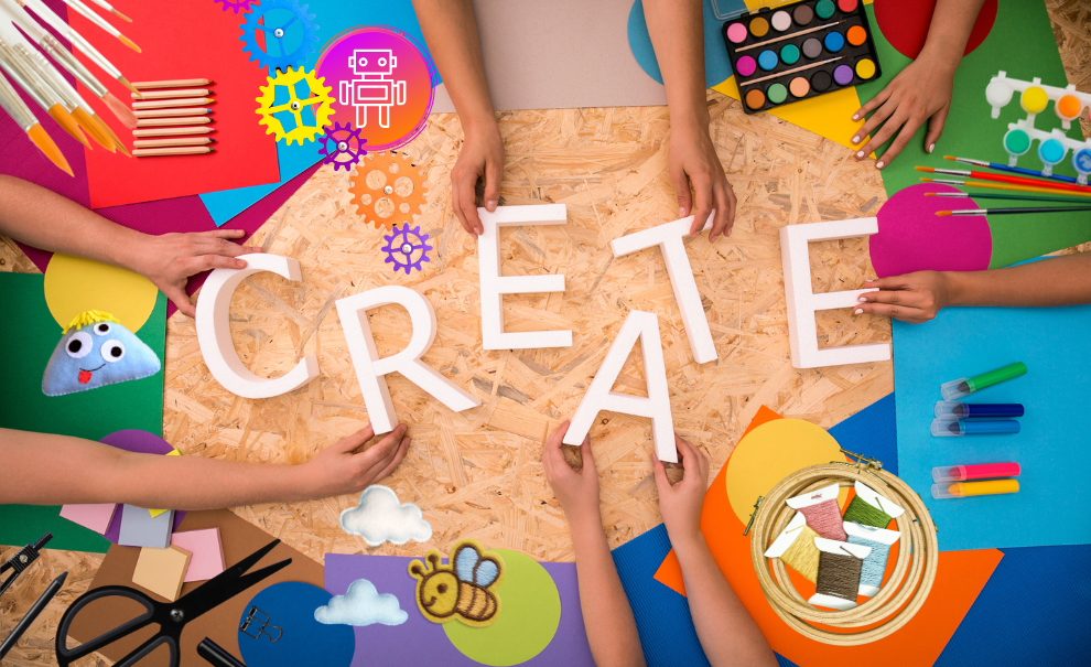 Birdseye view of a wooden table with craft supplies laid out and hands holding and interacting with the supplies. The white wooden letters that spell out the word CREATE is in the center.