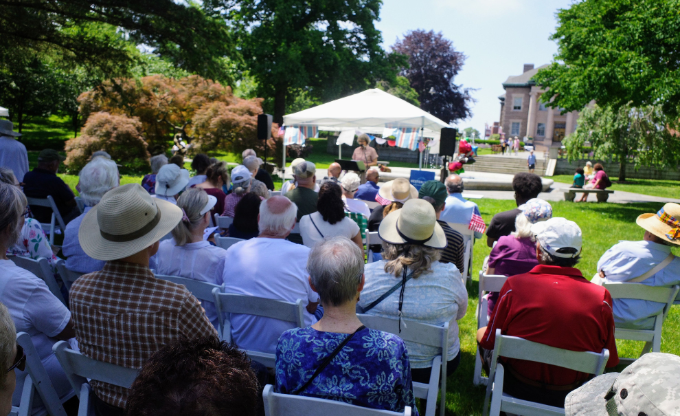 an audience watching a presenter in a tent out in the park