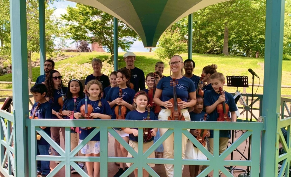Group of kids and adult woman instructor with violins in a bandshell out in the park