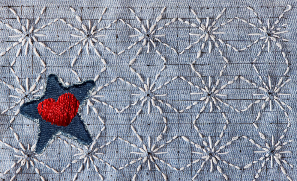 a close up of denim fabric embroidered with sashiko style stars in a repeating pattern and one dark denim star patch with a red embroidered heart.