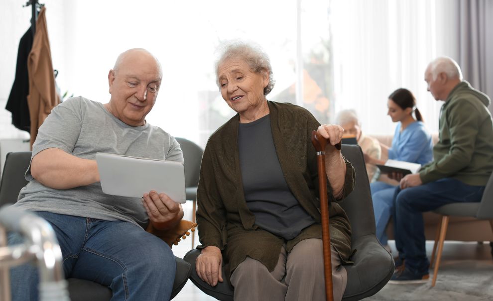 two older adults sit looking at a computer tablet together