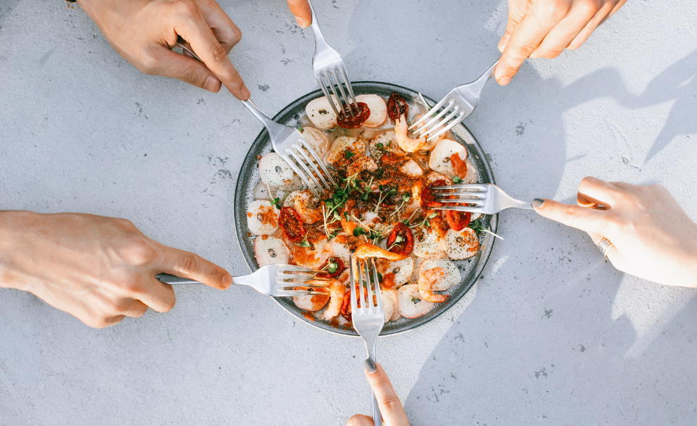 Hands reaching forks into bowl