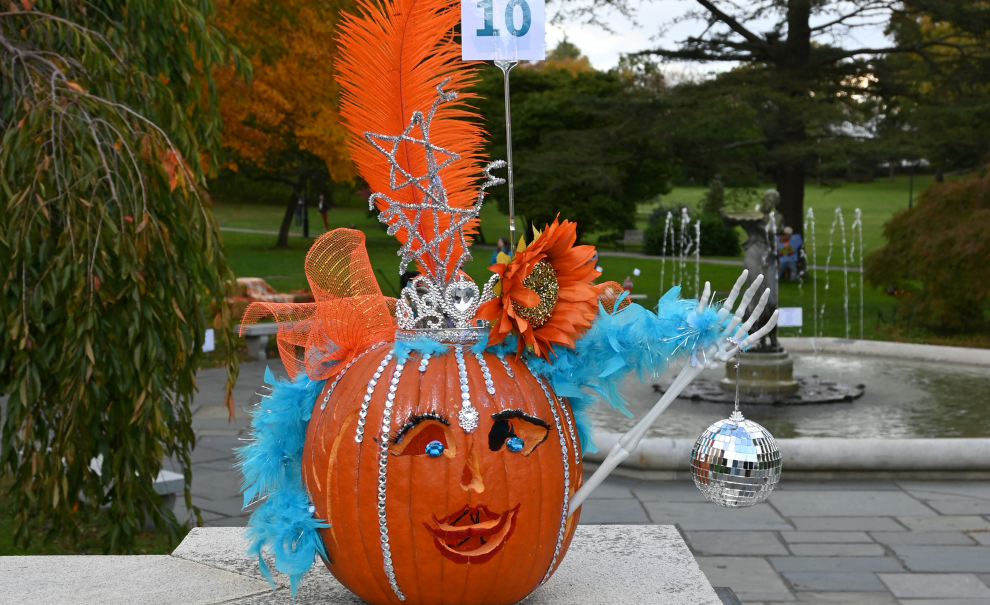 decorated orange pumpkin with blue feathers, orange flowers, silver tiara and disco ball and skeleton arm