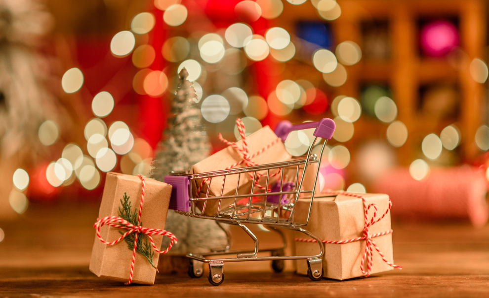 wrapped gifts with mini shopping cart and festive lights in the background