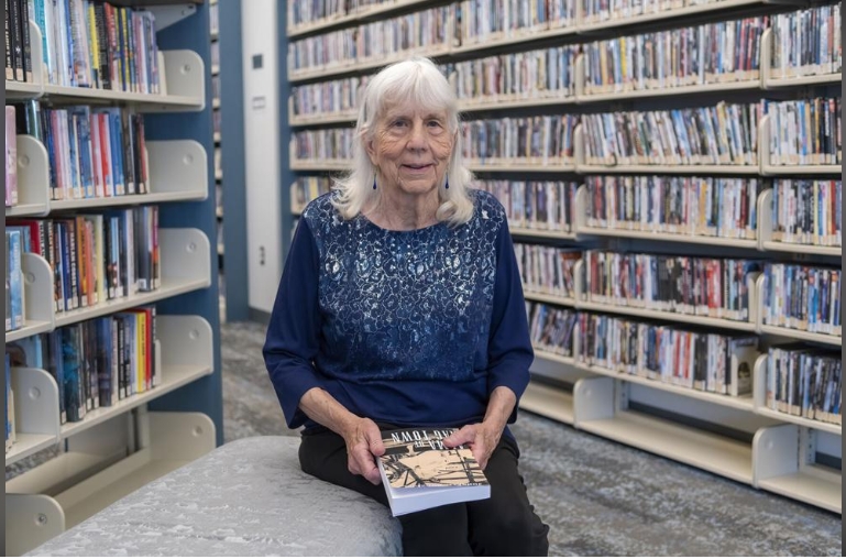 Author Johnette Rodriguez sitting with her book with a bookshelf backdrop