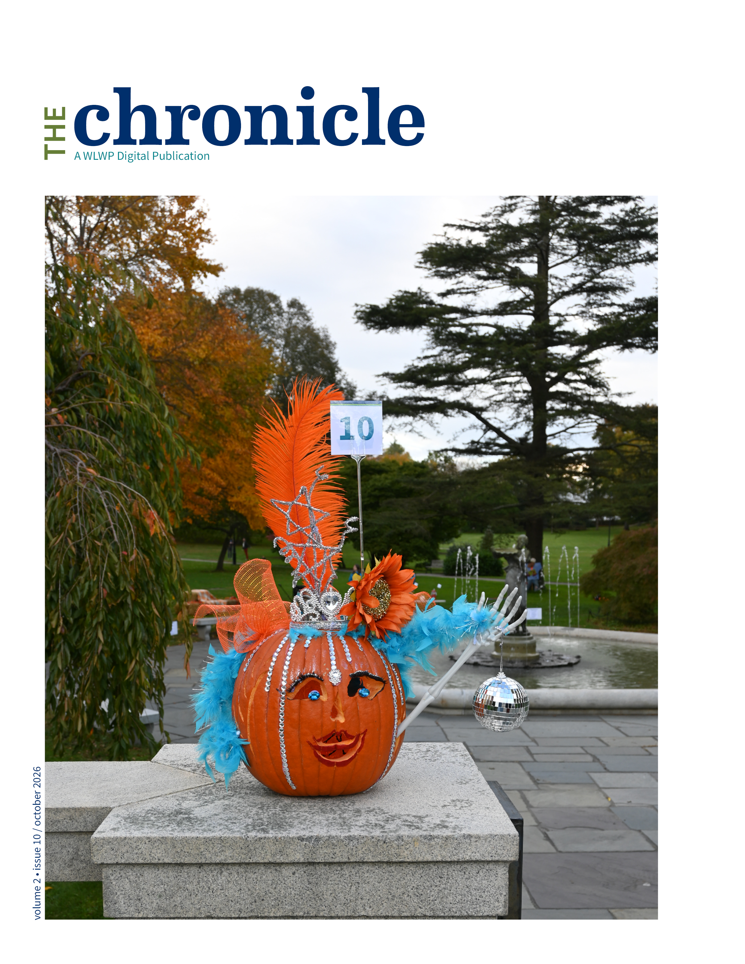 pumpkin decorated wtih orange and blue feathers and face with fountain and trees in a park in background