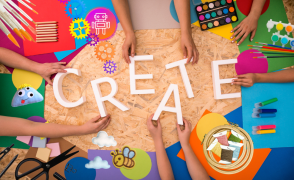 Birdseye view of a wooden table with craft supplies laid out and hands holding and interacting with the supplies. The white wooden letters that spell out the word CREATE is in the center.