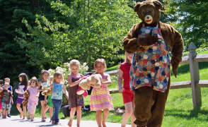 children following a bear in a musical parade