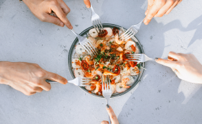 Hands reaching forks into bowl