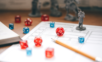 A dungeons and dragons character sheet laying on a table. On top of the sheet is a set of red and blue dice and a character miniature. 