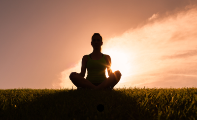 person meditating in front of an orange sunset