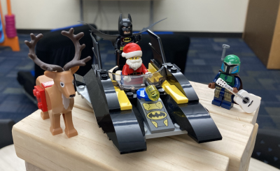 A LEGO Santa and Batman riding on a LEGO bat-boat. LEGO reindeer on their right and a LEGO Boba fett with a guitar on their left. 