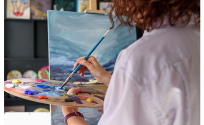 woman using a painting palette while in front of a canvas on an easel