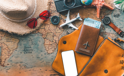 Close up of a map with travel related items spread across the surface such as a straw hat, sunglasses, a passport, a starfish, a camera, a phone, a travel wallet, and a watch.
