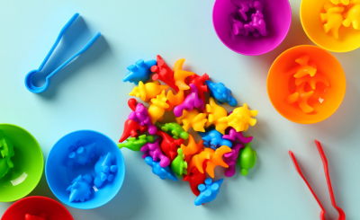 colorful dinosaur toys piled next to colorful cups and tweezers