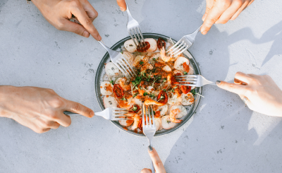 Hands reaching forks into bowl