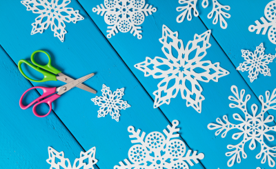 kid scissors pictured next to hand cut snowflakes on blue background
